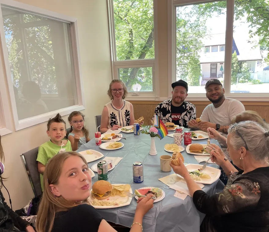 Children and adults around a table at the church BBQ, burgers and salads in front of them