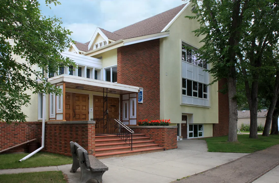 The front entrance of Highlands United Church on a summer day — brick steps up to the wooden doors, a flower box in bloom under the porch