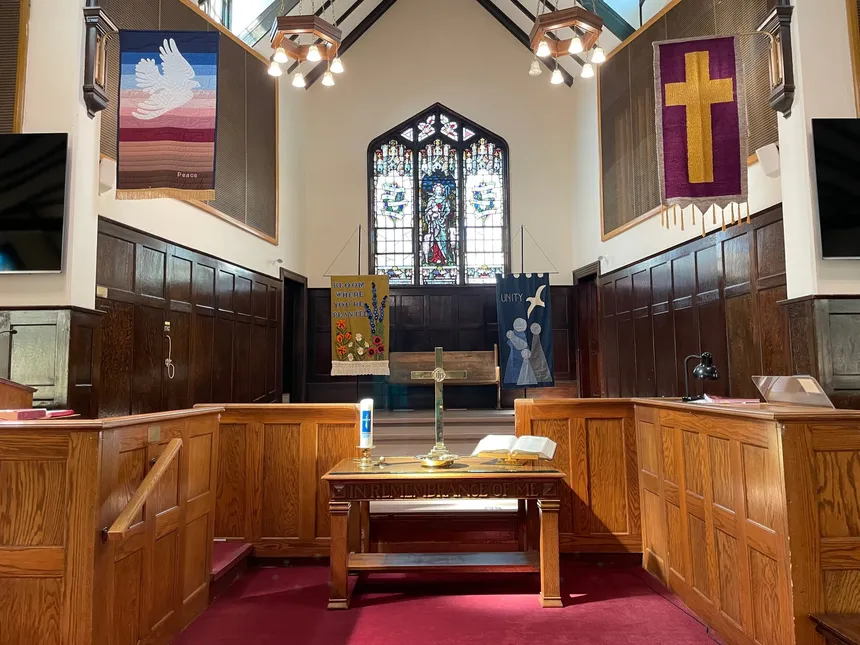 The chancel: the communion table with its cross and open Bible, the stained glass and dove banner above