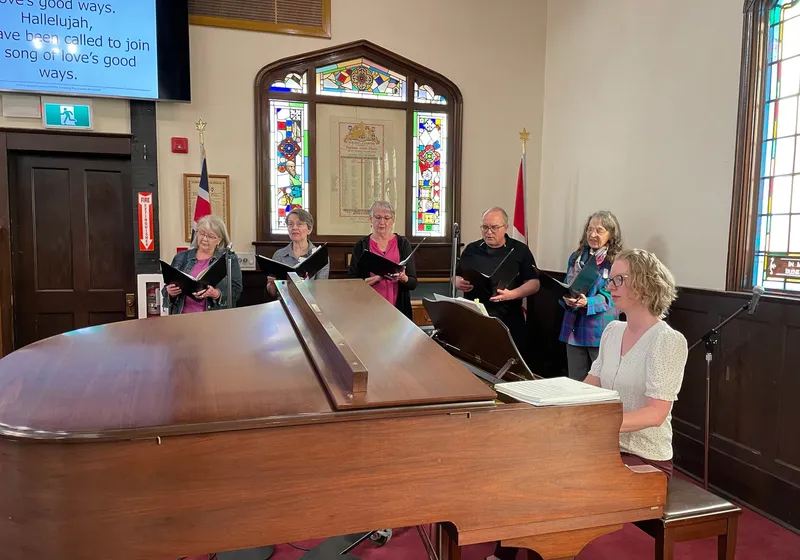 The choir singing around the grand piano before a service, the memorial window behind them