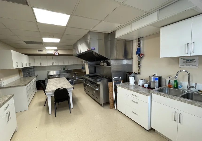 The commercial kitchen with stainless-steel range, hood, and prep tables