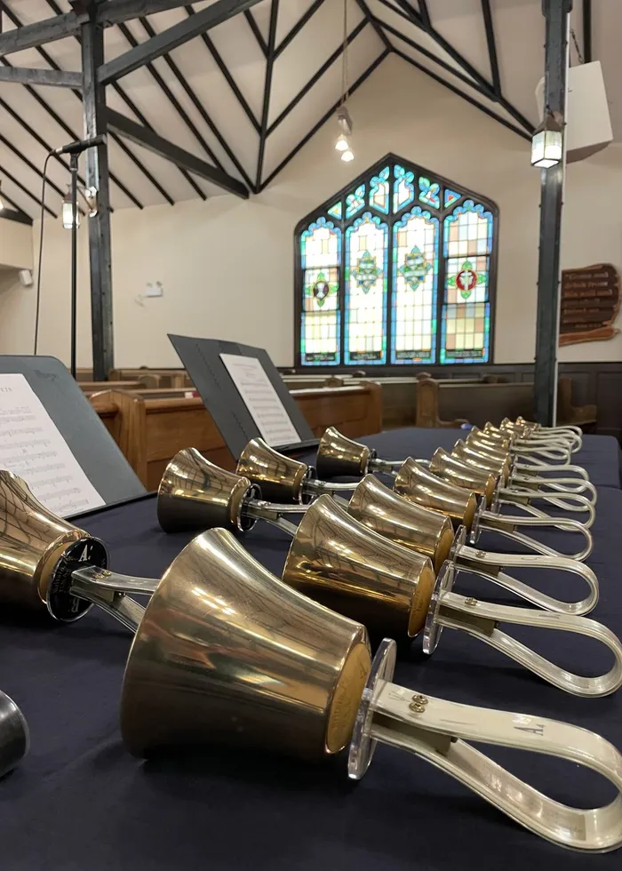 Rows of polished handbells laid out on the rehearsal table beneath a stained-glass window