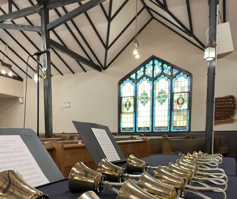 Rows of polished handbells laid out on the rehearsal table beneath a stained-glass window