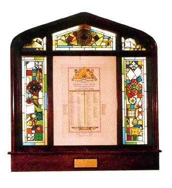 The Memorial Window: stained glass fragments from wartime Europe set in a dark arched wooden frame, surrounding an illuminated scroll of names