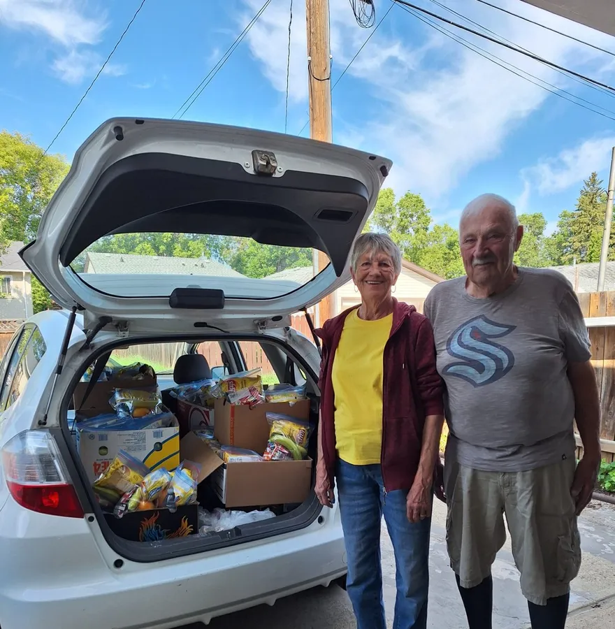 Two volunteers by a hatchback packed to the roof with donations, ready for delivery