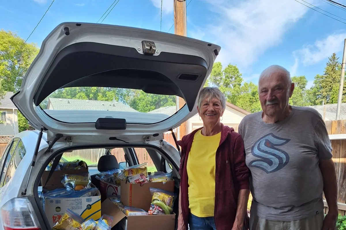 Two volunteers beside a car boot packed with donated groceries