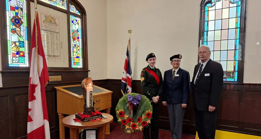 A Remembrance Day wreath and poppies beside the Memorial Window, with a cadet and veterans standing by the flags