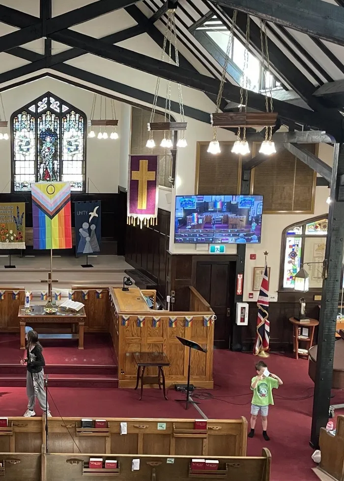 The congregation gathered in the sanctuary on a Sunday, rainbow flags by the chancel