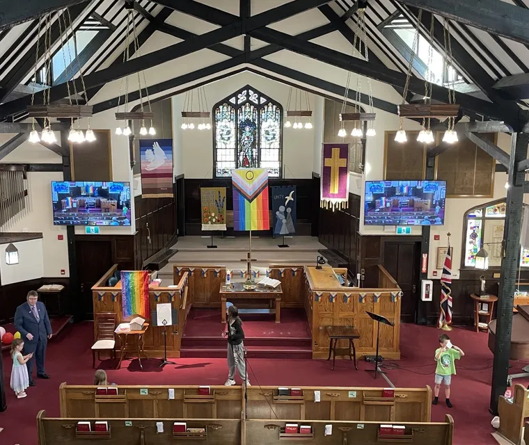 The congregation gathered in the sanctuary on a Sunday, rainbow flags by the chancel