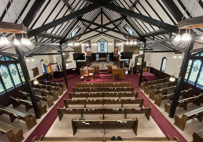 The sanctuary from the balcony — pews, timber trusses, and the chancel with its stained glass