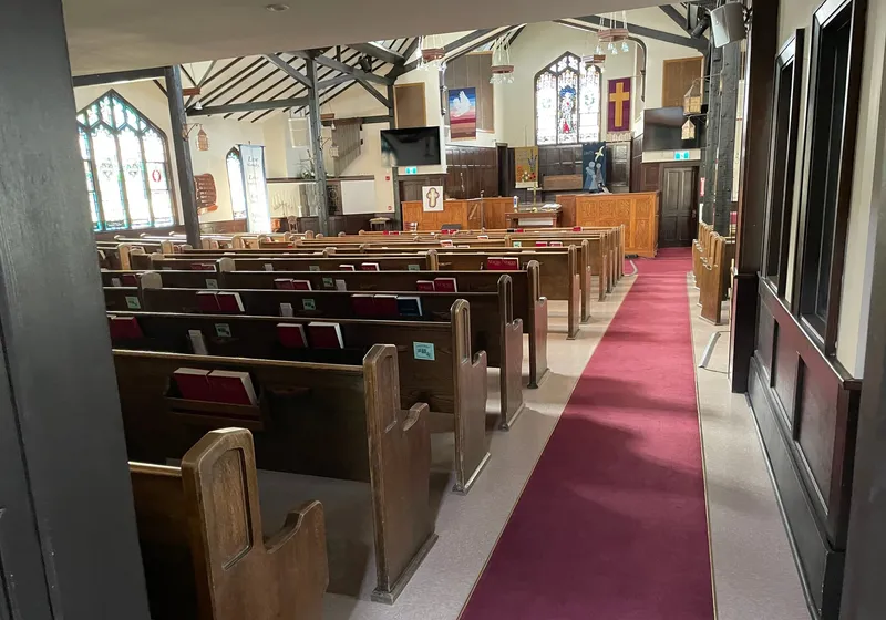 The sanctuary from a side aisle — oak pews, red carpet, and the stained glass at the front