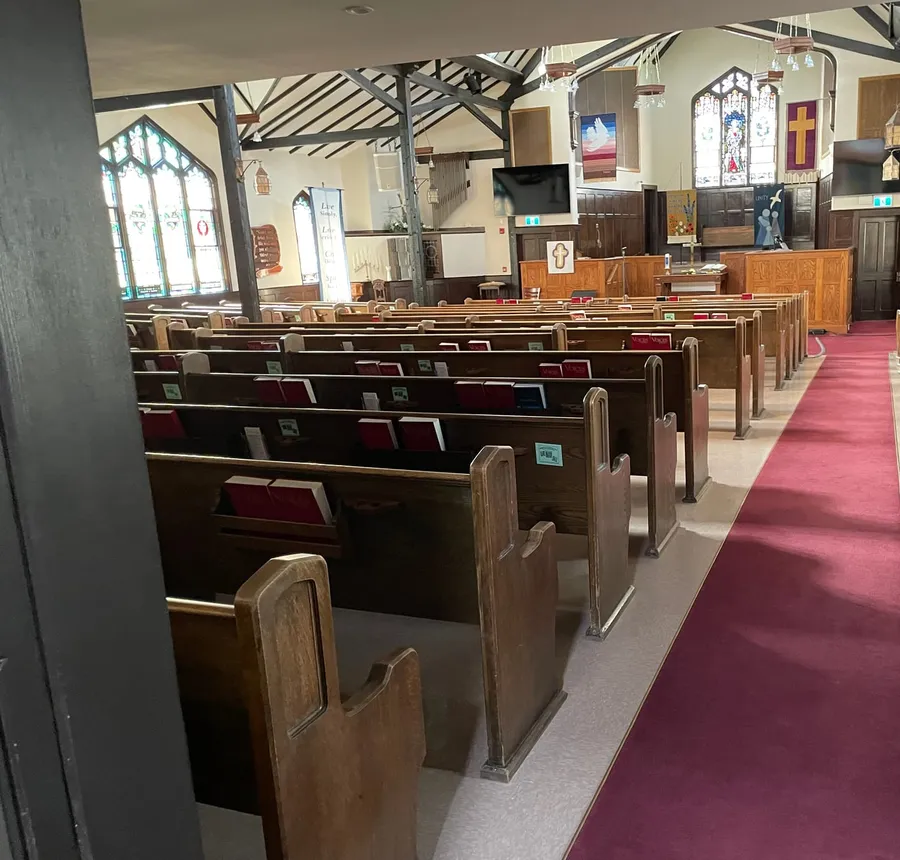 The sanctuary from a side aisle — oak pews, red carpet, and the stained glass at the front
