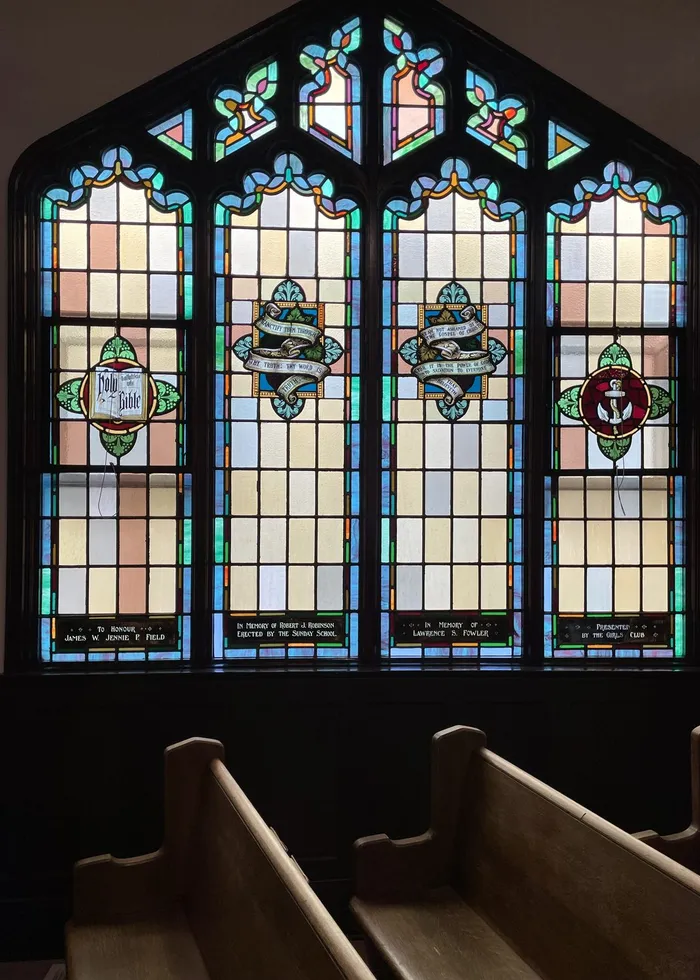Three arched stained-glass windows above the wooden pews of the sanctuary