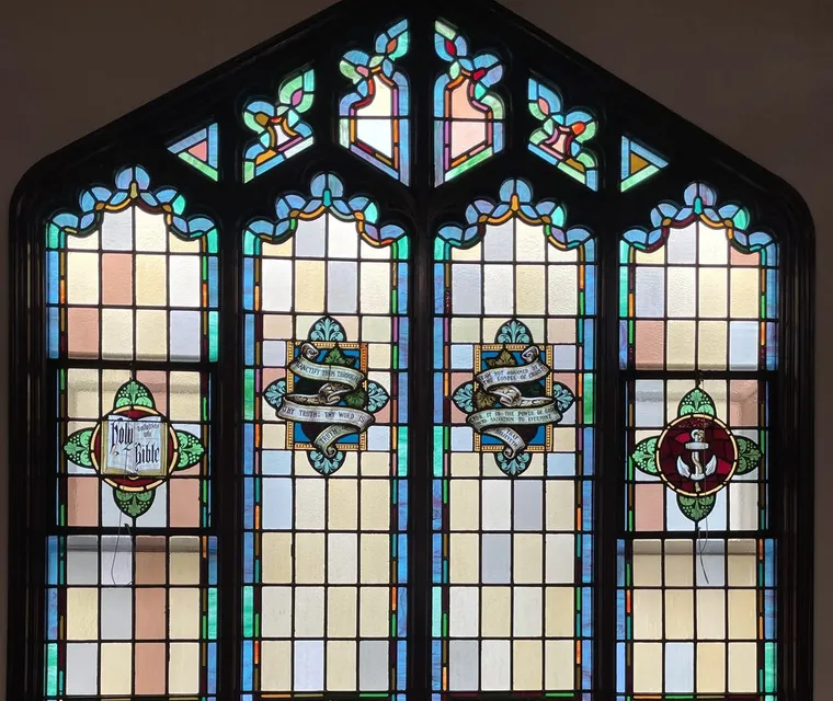 Three arched stained-glass windows above the wooden pews of the sanctuary